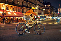Ein Mann mit oranger Jacke fährt in der Nacht auf einem E-Bike.